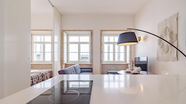 A modern kitchen with a built-in induction cooktop, large windows, and a dining area with a table and chairs. - Tower 5F in Oporto With 1 Bathrooms (Porto)