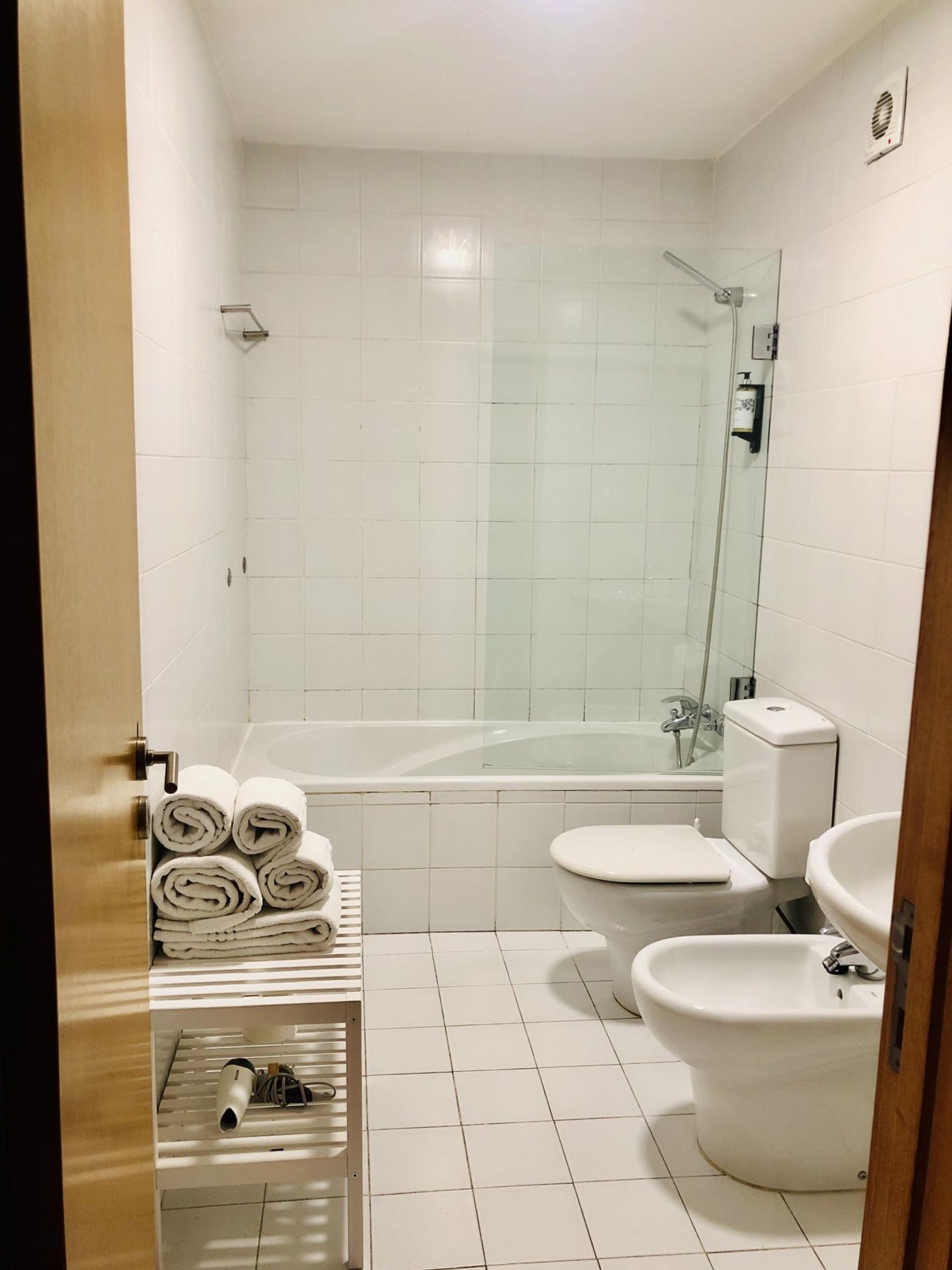 A modern bathroom with a glass-enclosed shower, a bathtub, a toilet, and a sink. There are towels stacked on a shelf.