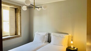 Ein Schlafzimmer mit einem Bett, einem Fenster, einer Wandleuchte und einem Nachttisch mit Lampe.