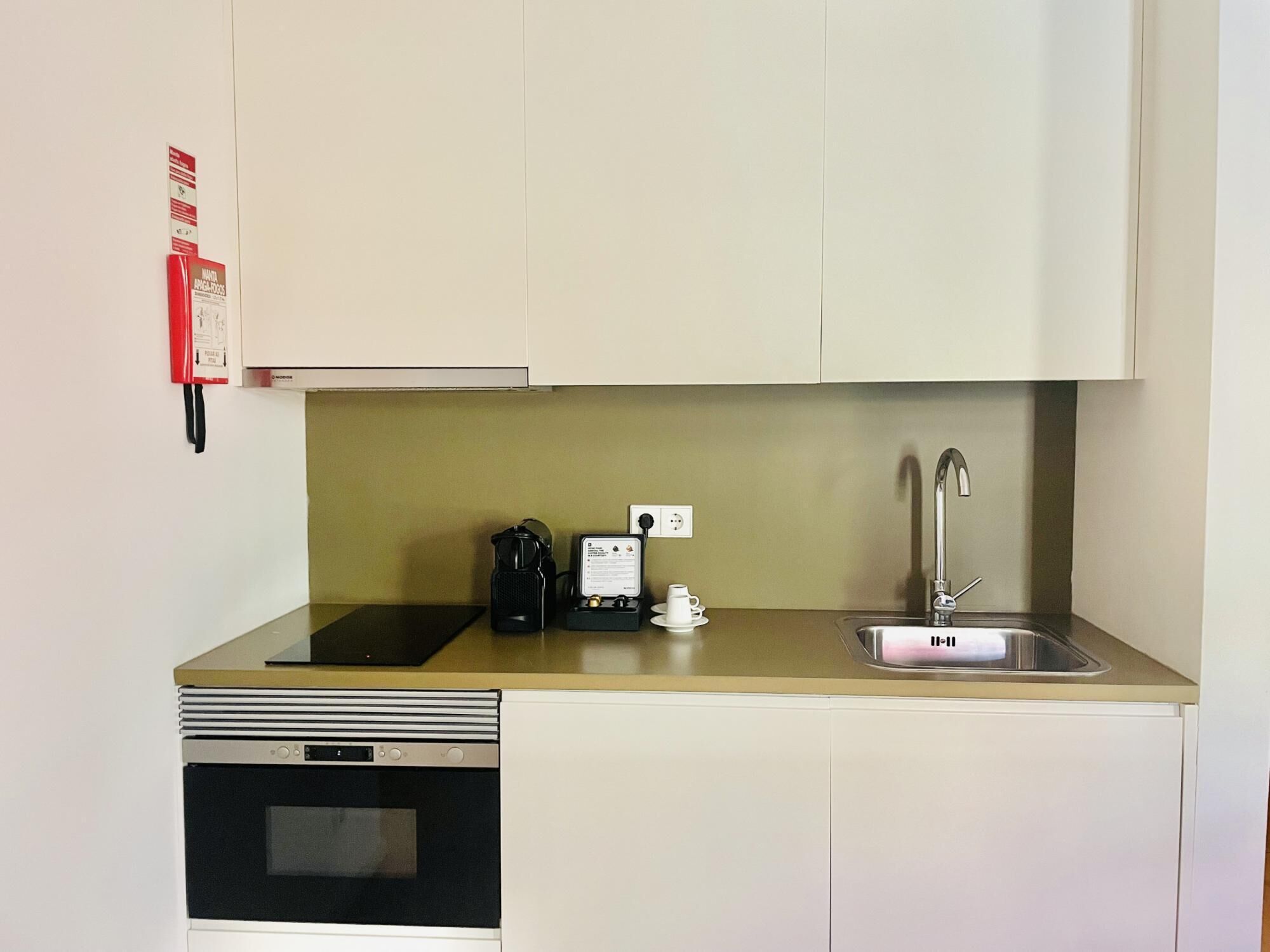 A compact kitchenette with a built-in oven, a coffee maker, a kettle, a small sink, and a power outlet.