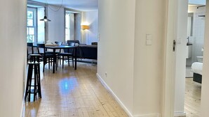Un pasillo amplio con piso de madera, un comedor con mesa y sillas, y vistas a un dormitorio con cama y baño.