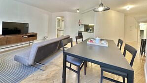 Una sala de estar moderna con un televisor grande, sofá, mesa de comedor y sillas.