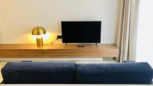 A modern living room with a flat-screen TV on a wooden stand, a gold lamp, and a dark blue sofa. - Downtown 2A in Oporto (Porto)