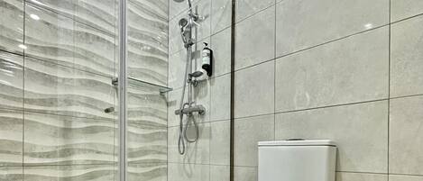 Une salle de bain moderne avec une douche à parois de verre, des toilettes blanches et un sol en marbre.
