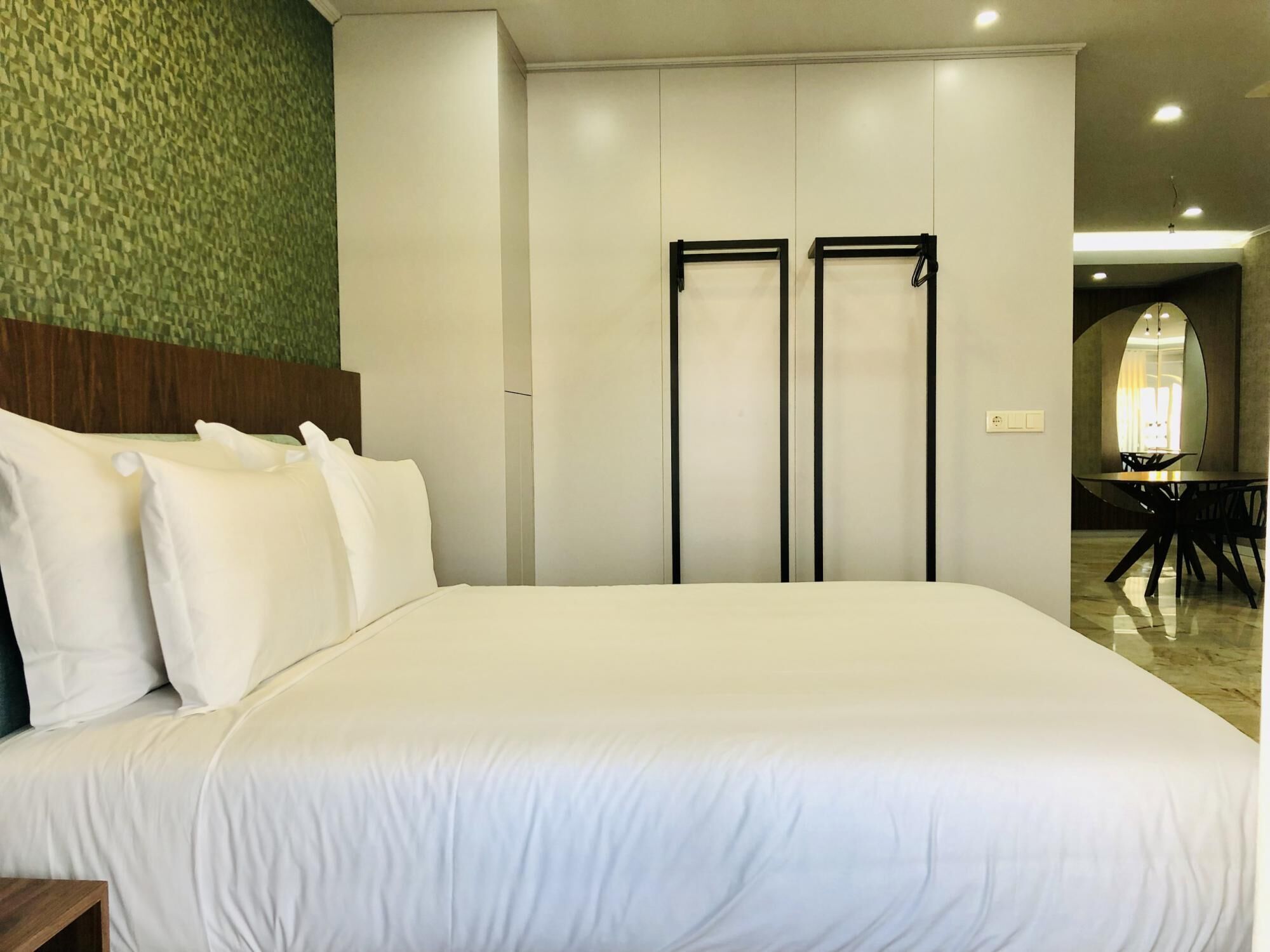 Ein Hotelzimmer mit einem großen Bett, einem Holzkopfende, einer Wand mit grüner Struktur und einem Essbereich mit rundem Tisch und Stühlen.