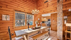 Ein rustikales Holzhaus-Interieur mit einer Steinsäule, einem Esstisch mit Bänken, einer Kandelaber und einer Küchenzeile.