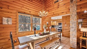 Ein rustikales Holzhaus-Interieur mit einer Steinsäule, einem Esstisch mit Bänken, einer Kandelaber und einer Küchenzeile.