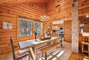 Ein rustikales Holzhaus-Interieur mit einer Steinsäule, einem Esstisch mit Bänken, einer Kandelaber und einer Küchenzeile.