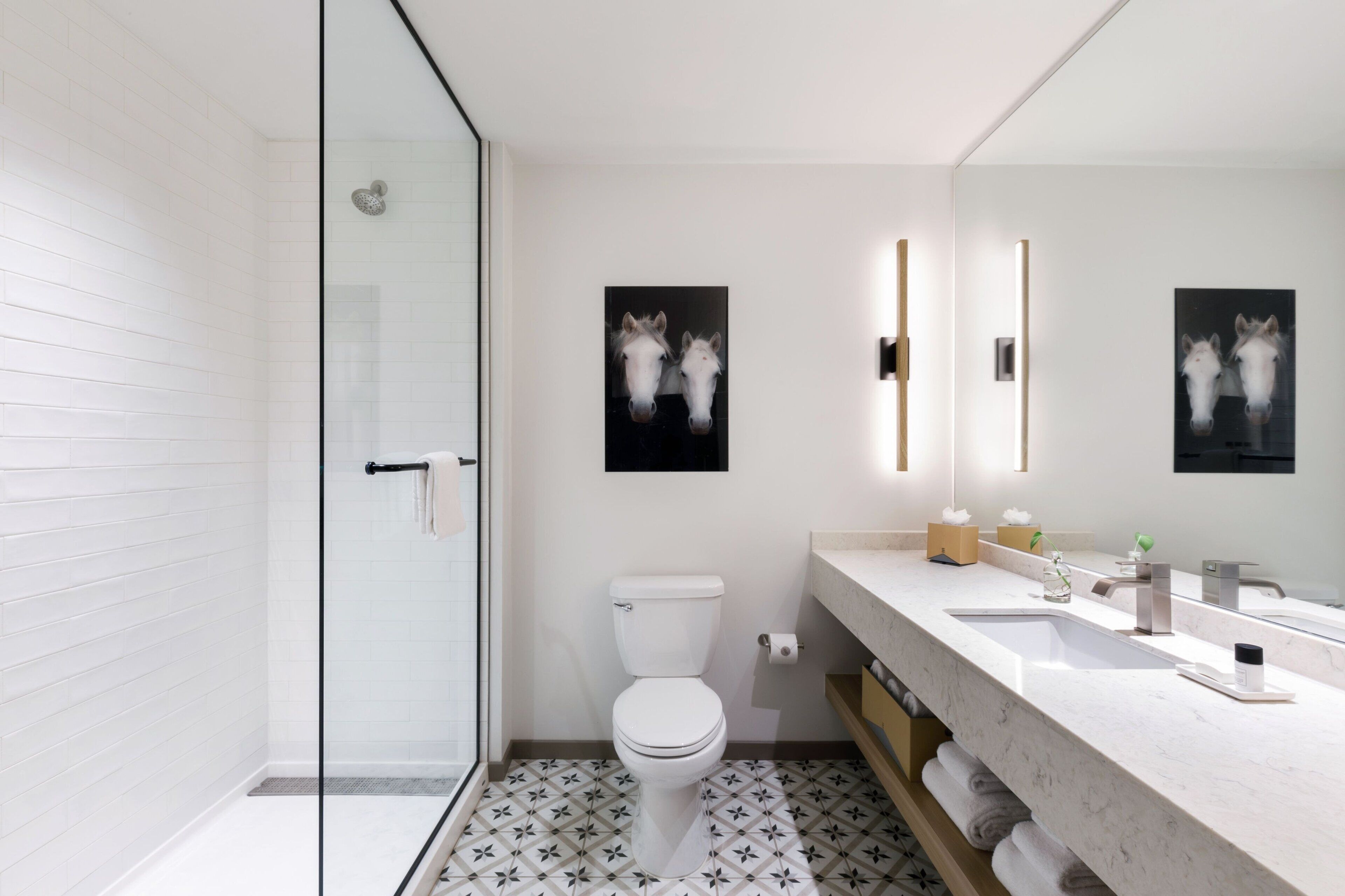 Un baño moderno con cabina de ducha de vidrio, inodoro blanco y lavamanos de mármol con un espejo grande.