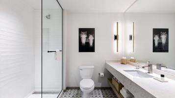 Un baño moderno con cabina de ducha de vidrio, inodoro blanco y lavamanos de mármol con un espejo grande.