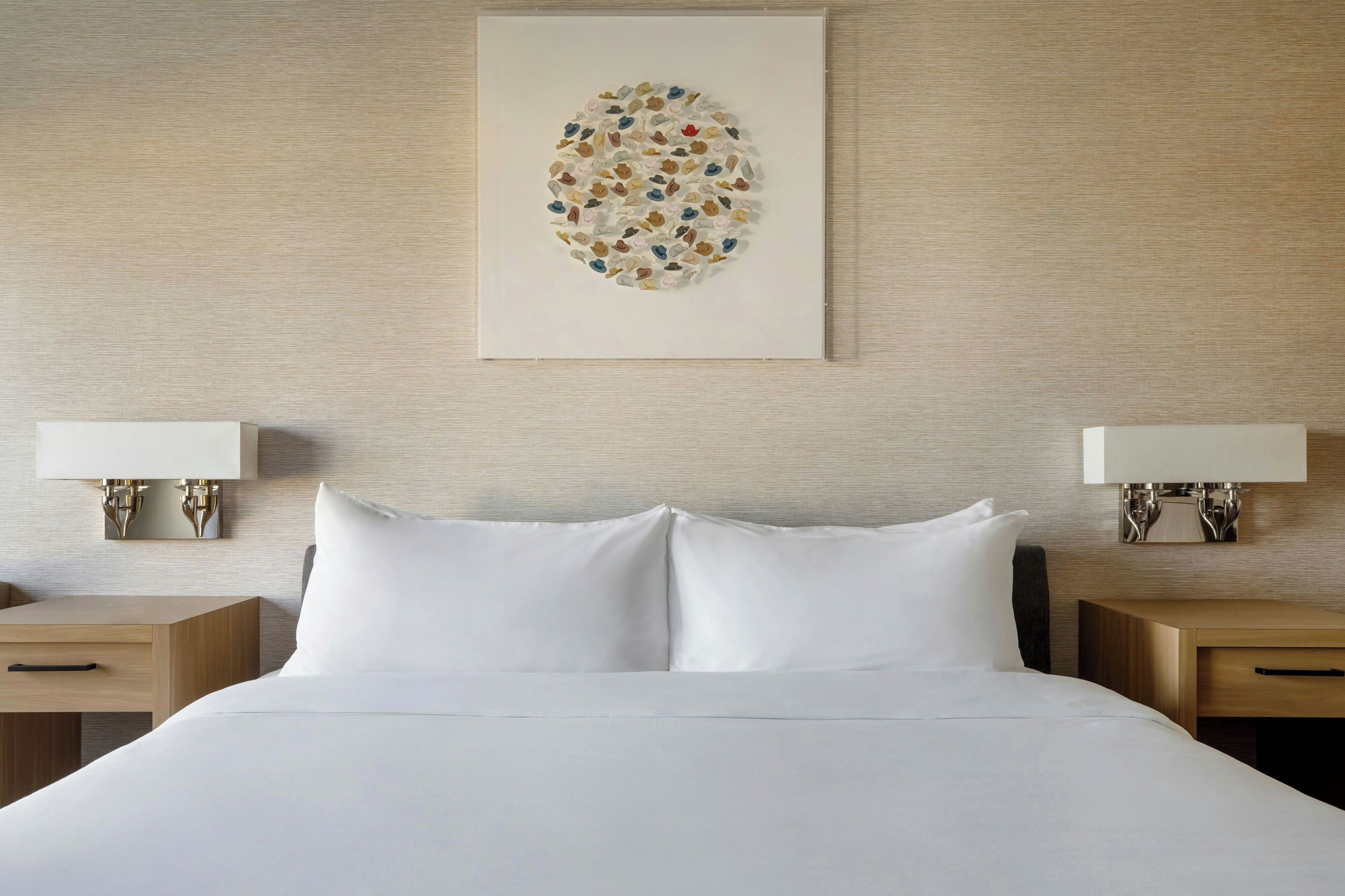 Habitación de hotel con una cama bien hecha, dos mesitas de noche con lámparas y una obra de arte colgada en la pared.