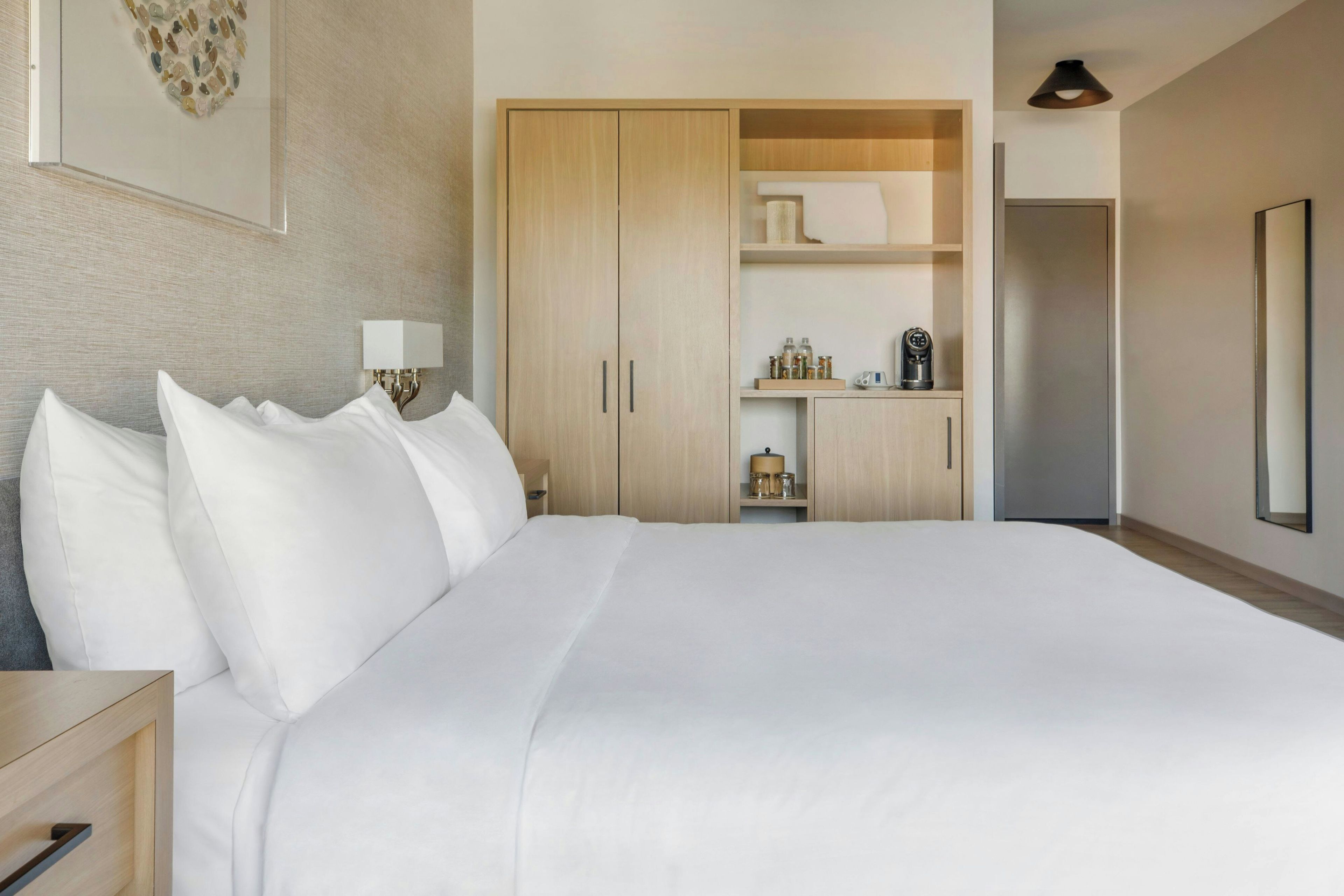 A hotel room with a large bed, a wardrobe, a bedside table with a lamp, and a mirror on the wall.