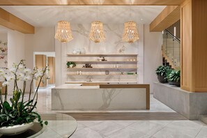 A modern reception area with a marble counter, wooden shelving, and hanging pendant lights. - NOUN Hotel, Norman, a Tribute Portfolio Hotel (Norman)