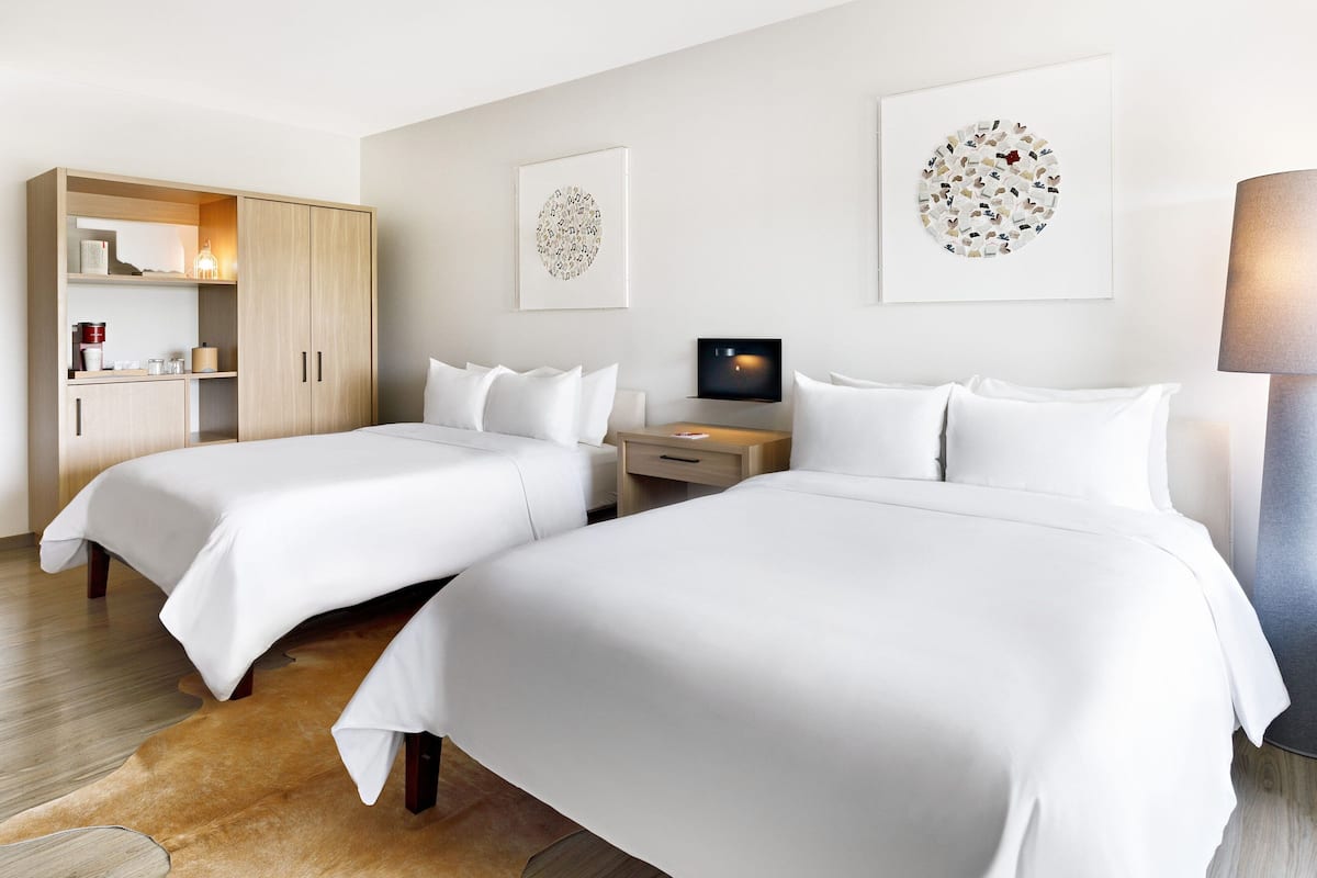 A hotel room with two beds, a wardrobe, a desk, and artwork on the walls.