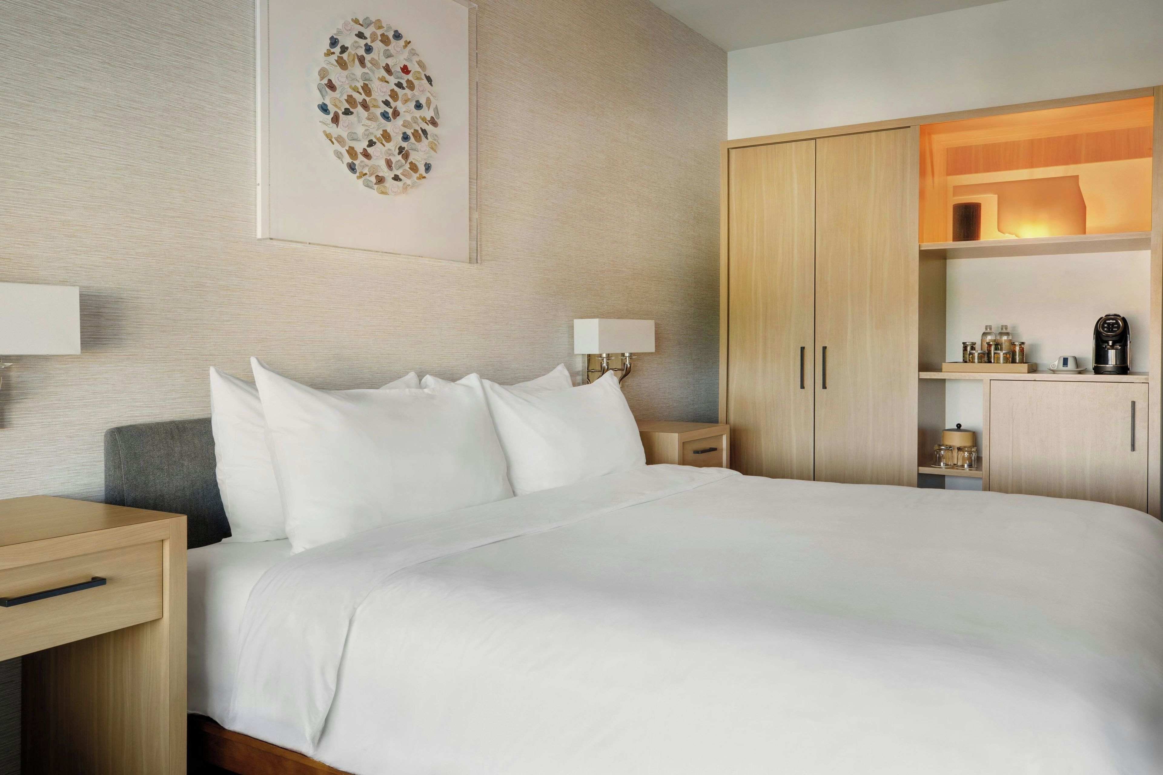 A hotel room with a large bed, bedside tables, a wardrobe, and a wall-mounted artwork.