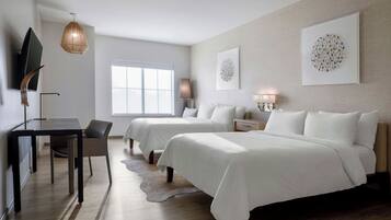 A modern hotel room with a desk, two beds, a large window, and artwork on the walls.