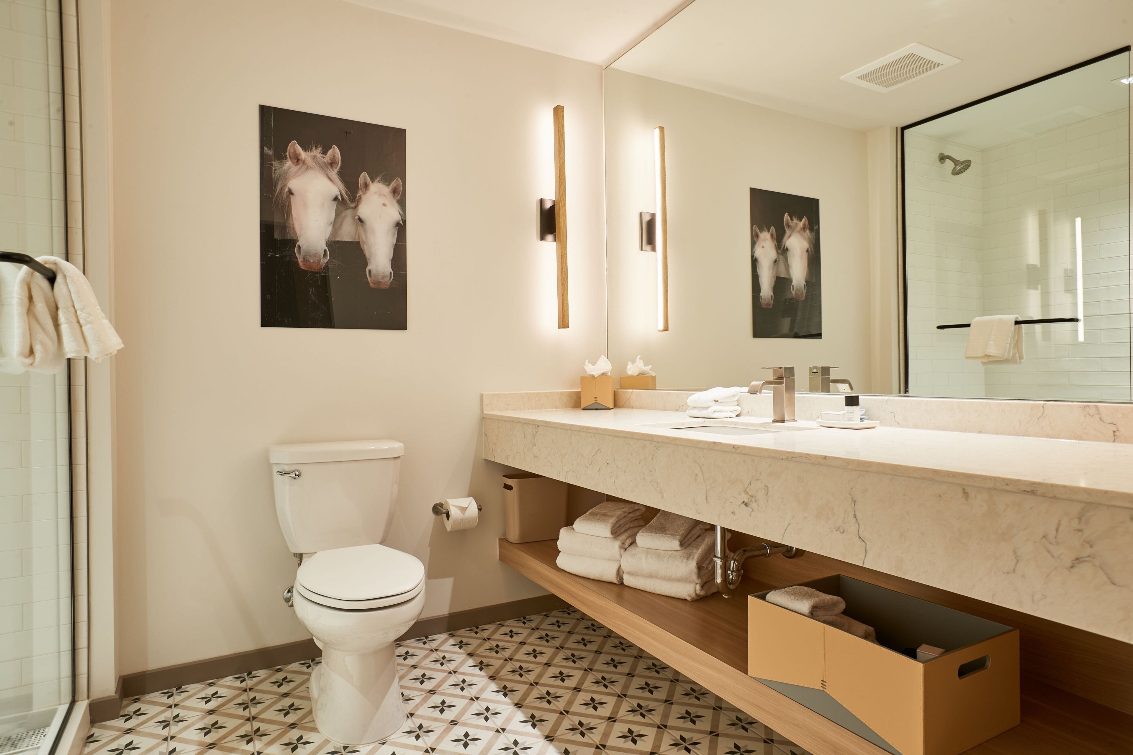 Un baño moderno con inodoro, lavamanos con encimera de mármol y dos espejos fijados a la pared.
