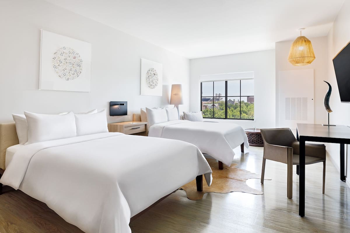 A hotel room with two beds, a desk, a chair, a TV, and artwork on the walls.