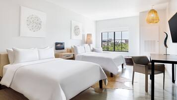 A hotel room with two beds, a desk, a chair, a TV, and artwork on the walls.