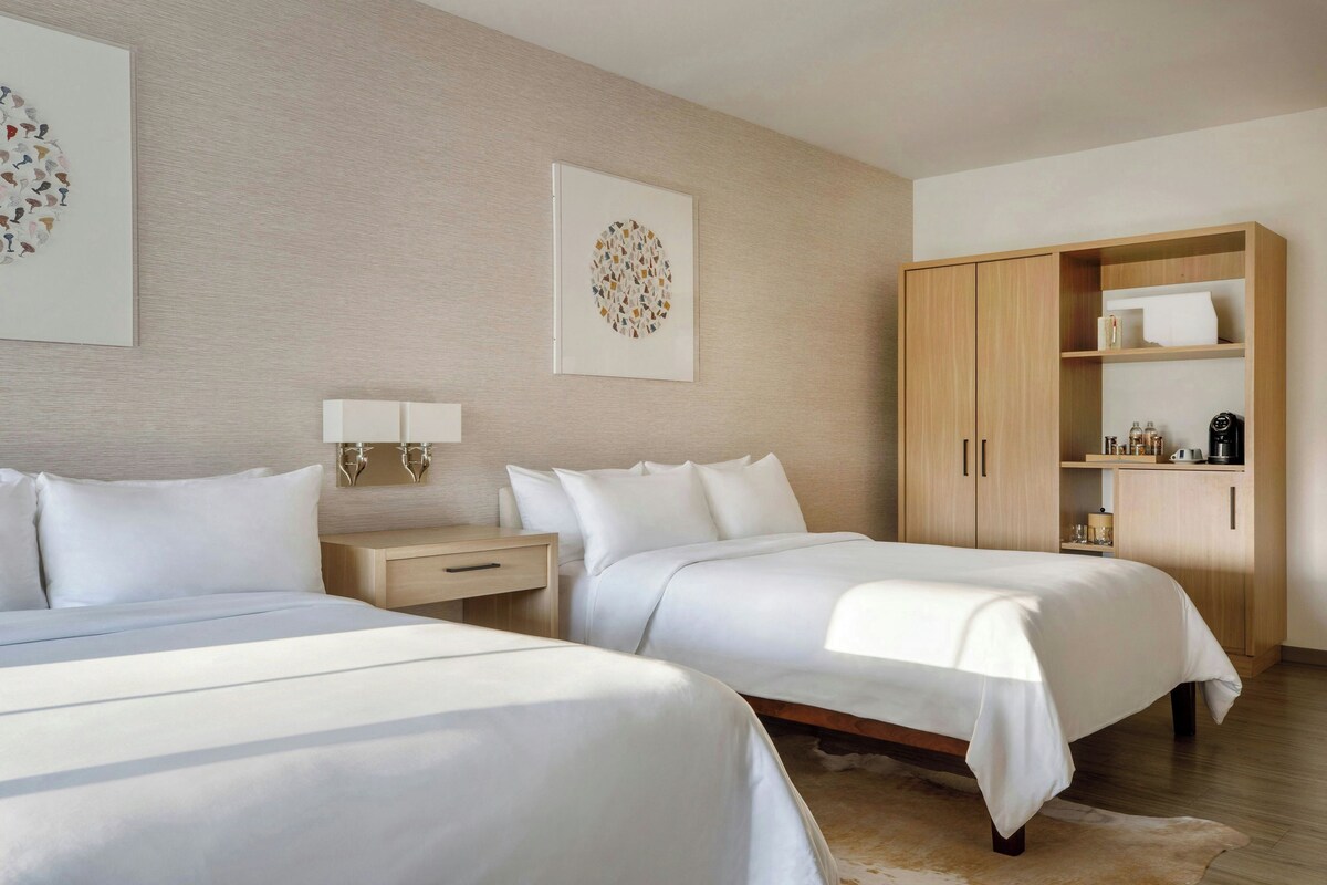 A hotel room with two beds, a wooden wardrobe, a nightstand, and wall art.