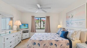 Quarto de hotel com cama, televisão, escrivaninha e janela com cortinas.