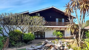 Une maison à deux étages dotée d’un balcon, entourée de différentes plantes et d’un petit jardin.