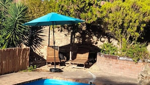 Une piscine avec un parasol bleu, entourée d’un mur de briques et de verdure.