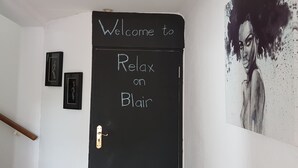 Une porte sur laquelle on peut lire « Bienvenue à Relax on Blair », un tableau noir et un tableau encadré.
