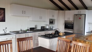 Une cuisine moderne avec des meubles blancs, une cuisinière à gaz, un four à micro-ondes et un réfrigérateur. On y trouve des chaises en bois et une petite table.