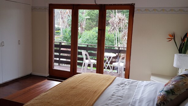 Une chambre à coucher avec un lit, un banc en bois, une armoire blanche et un balcon donnant sur un paysage verdoyant.