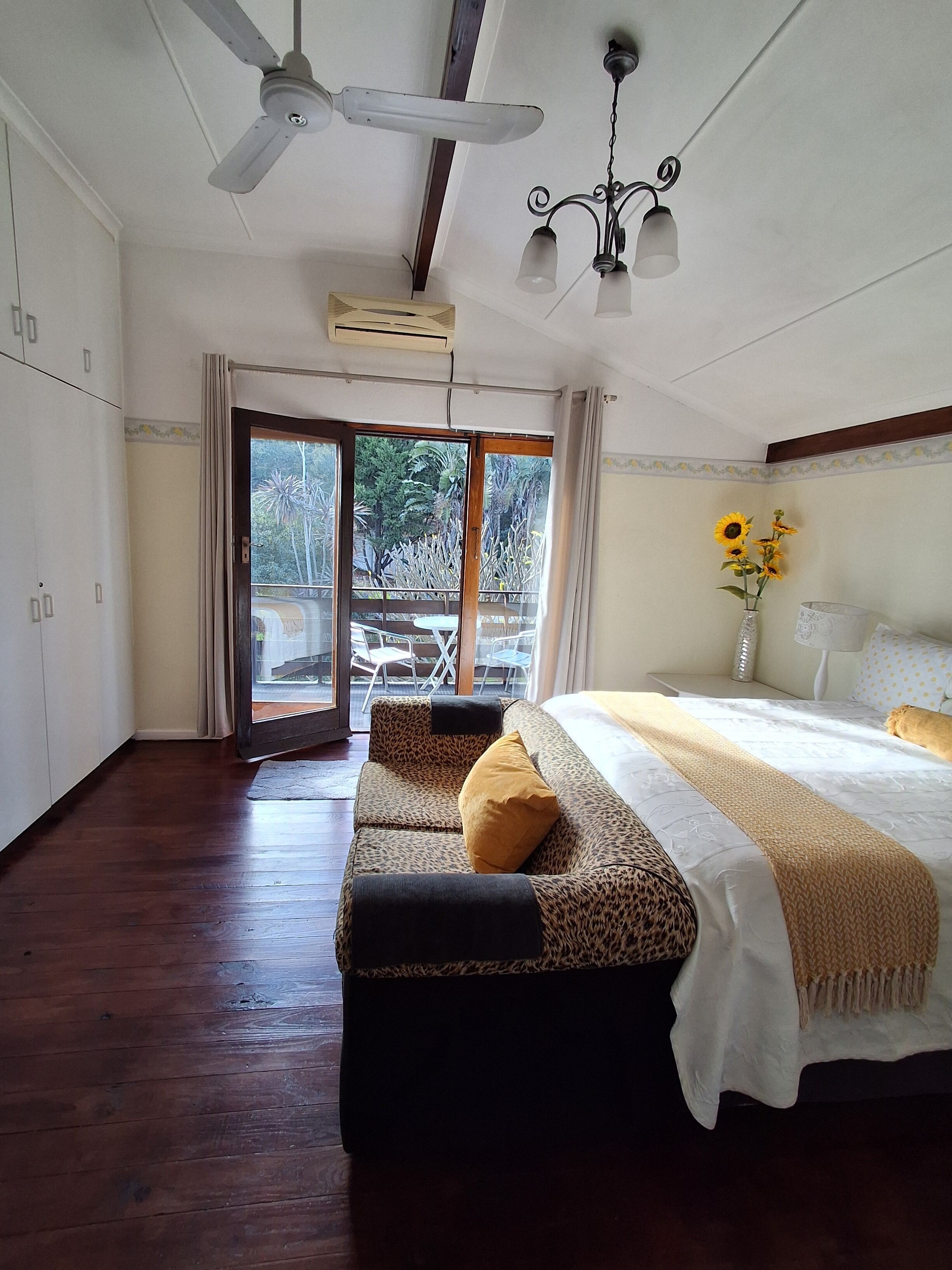 A bedroom with a bed, a bench, a ceiling fan, and a view through a glass door.