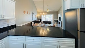 A modern kitchen with white cabinets, a black countertop, and a dining area with a table and chairs.