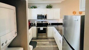 A narrow kitchen with white cabinets, a stainless steel refrigerator, a microwave, and an oven.