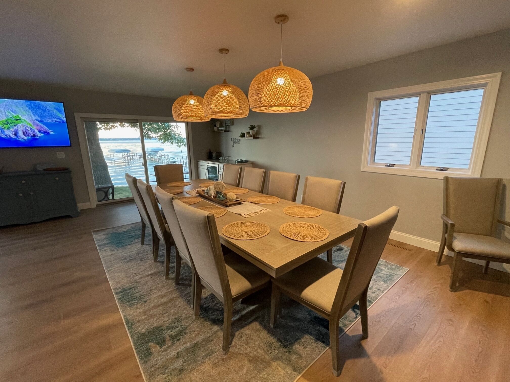Un espace repas avec une table en bois, des chaises de couleur beige et des suspensions lumineuses en fibres tressées.