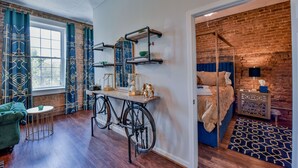 Una habitación con una bicicleta como mesa, una cama con cabecera azul y una pared de ladrillo.