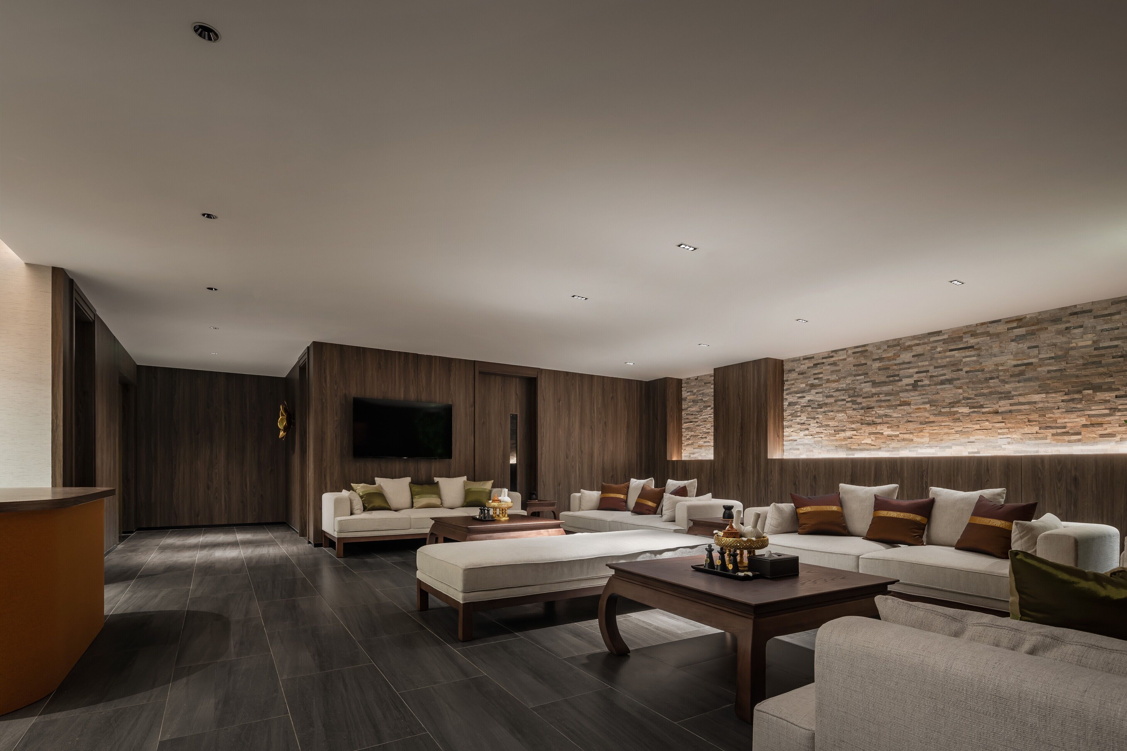 A modern living room with dark wood flooring, a large sectional sofa, a coffee table, and a stone accent wall.