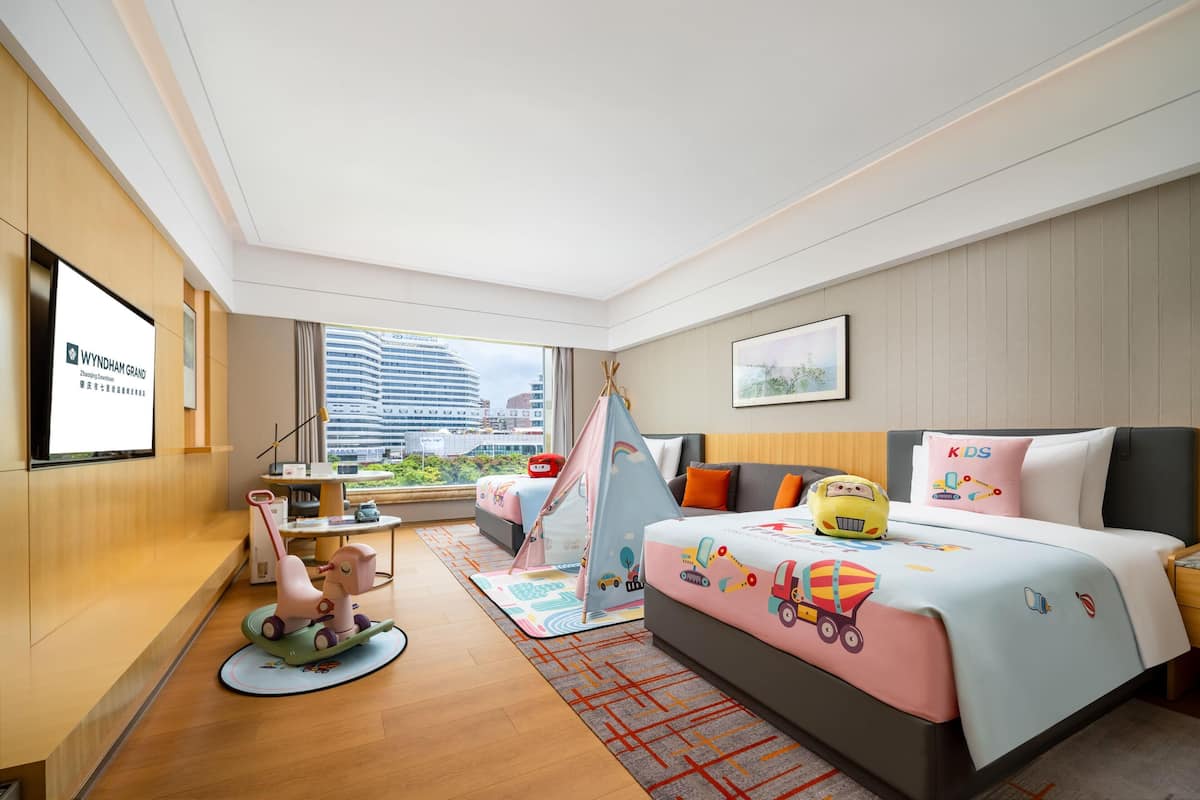 Habitación de hotel con cama, escritorio, silla, caballito de madera y ventana con vista a la ciudad.