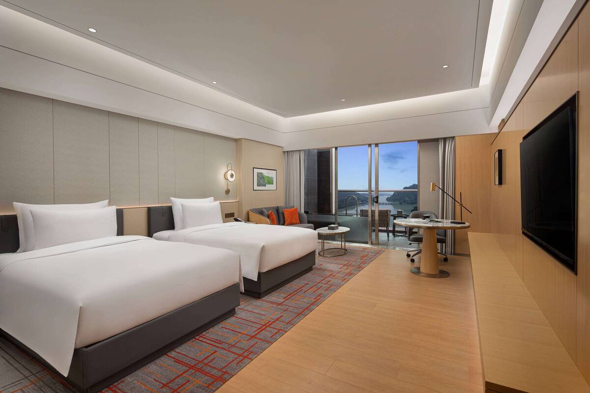 Una habitación de hotel moderna con dos camas, un escritorio, una silla y un televisor grande.