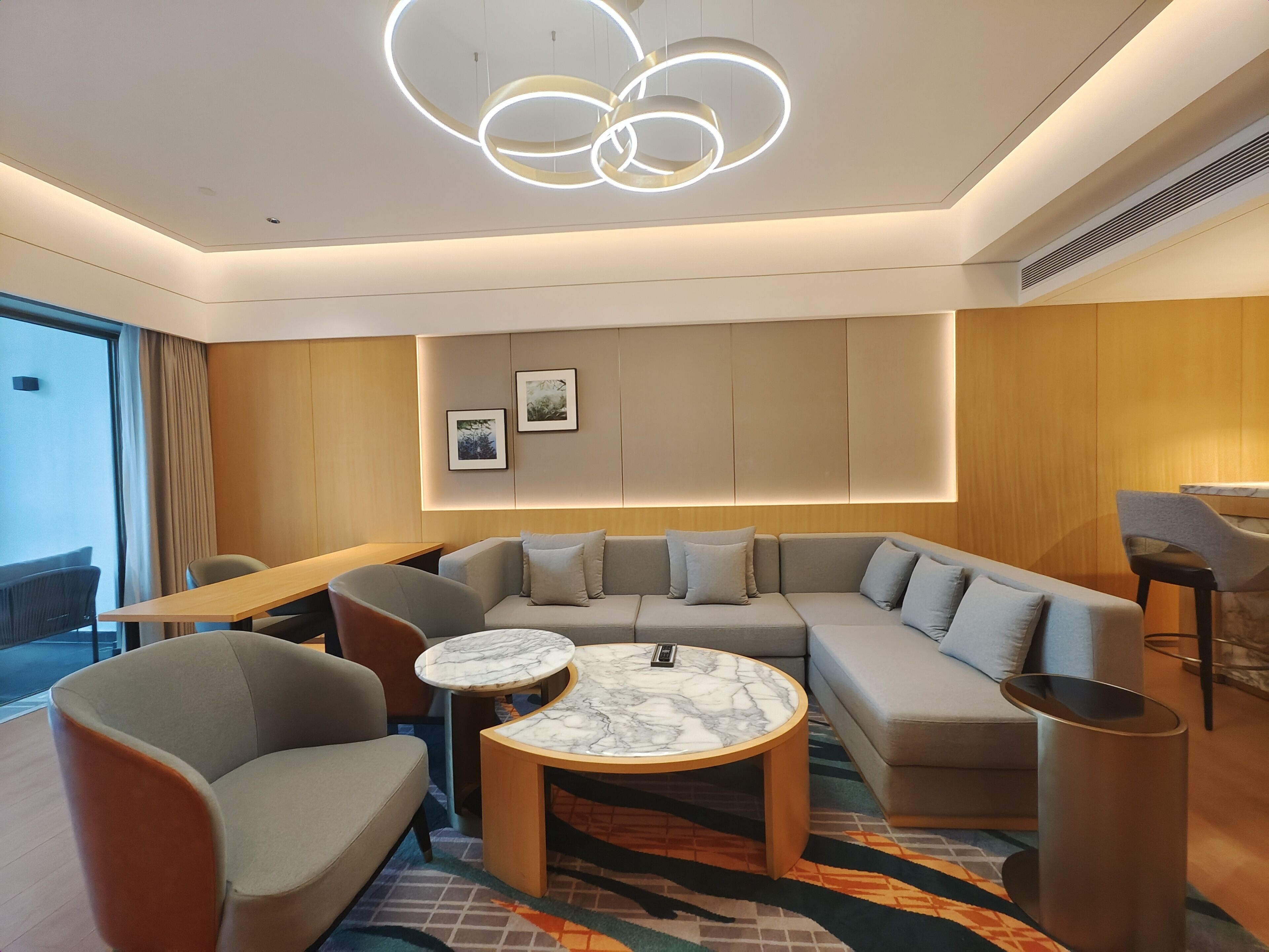 A modern living room with a sectional sofa, two armchairs, a marble coffee table, and a unique circular light fixture.