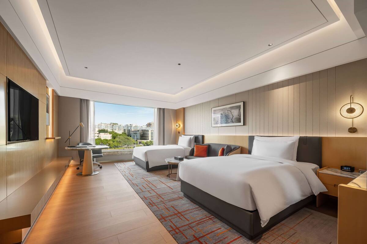 Una habitación de hotel moderna con dos camas, un escritorio, un televisor y vistas a la ciudad.