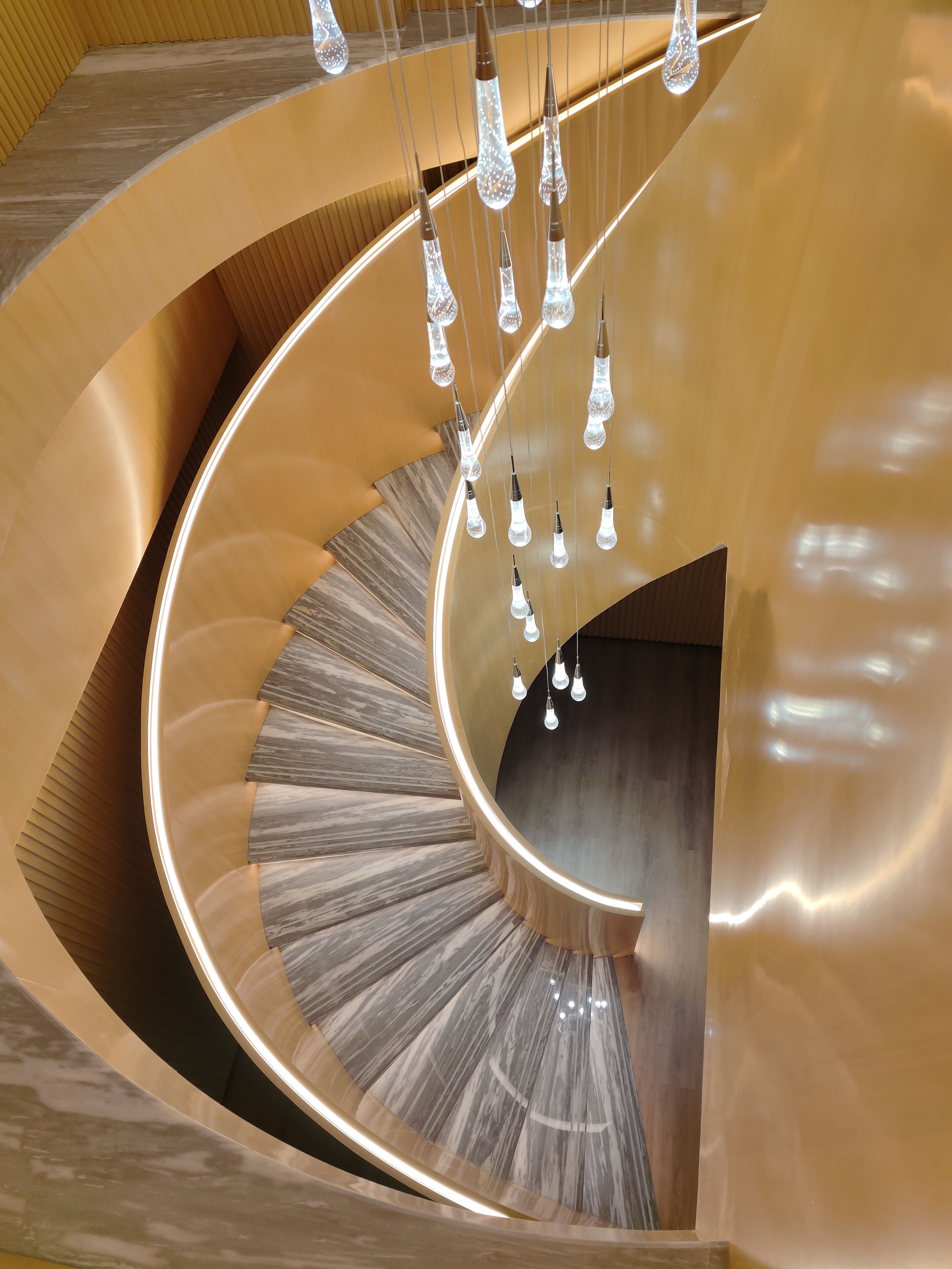 A spiral staircase with a polished wooden finish and hanging crystal light fixtures.