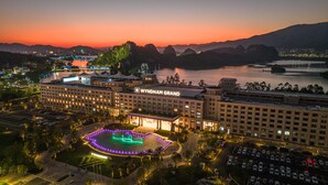 A large hotel with a prominent sign, a landscaped pool area, and surrounding mountains. - Wyndham Grand Zhaoqing Downtown (Zhaoqing)