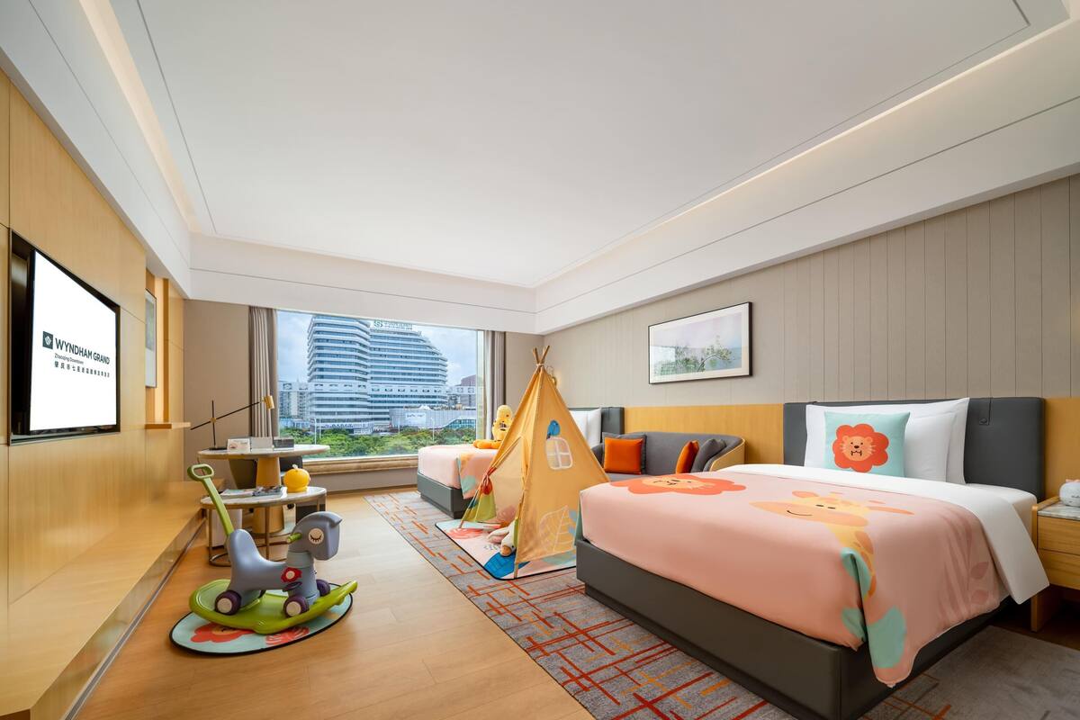 Habitación de hotel con cama, escritorio, silla, un coche de juguete, una tienda de campaña y vistas a la ciudad.