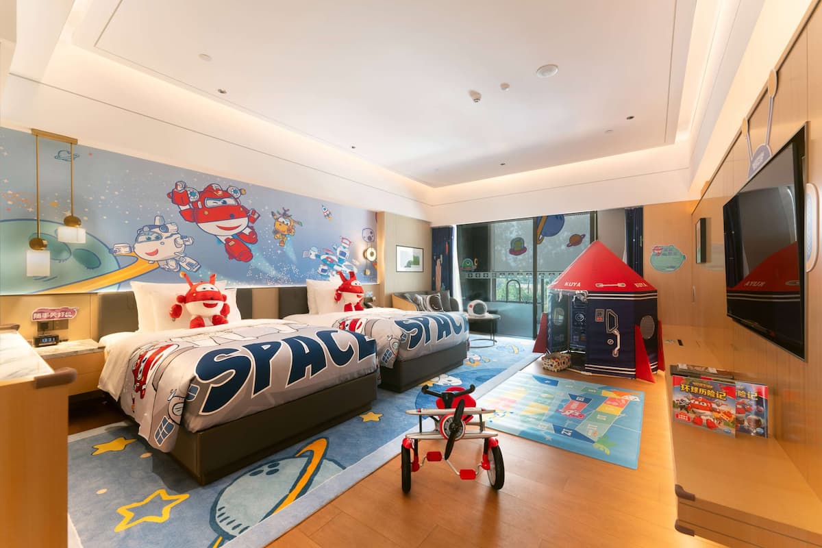 Habitación infantil con mural de temática espacial, literas, zona de juegos con un coche de juguete y televisor montado en la pared.