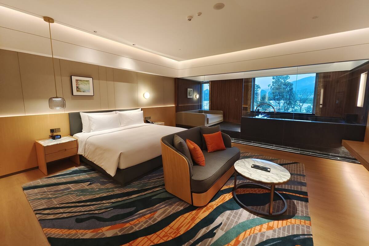 Una habitación de hotel moderna con una cama grande, un sofá, una mesita y vistas al exterior.
