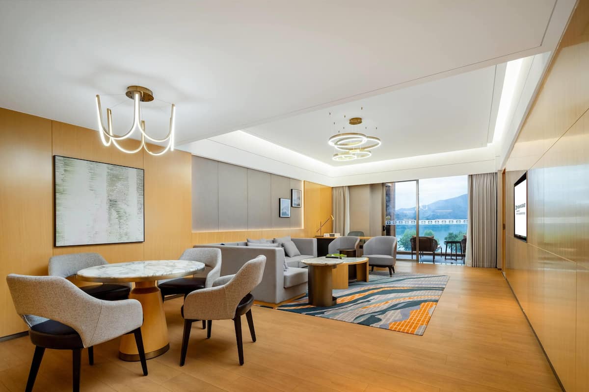 Una habitación de hotel moderna con comedor, un conjunto de sofás y vistas a las montañas.