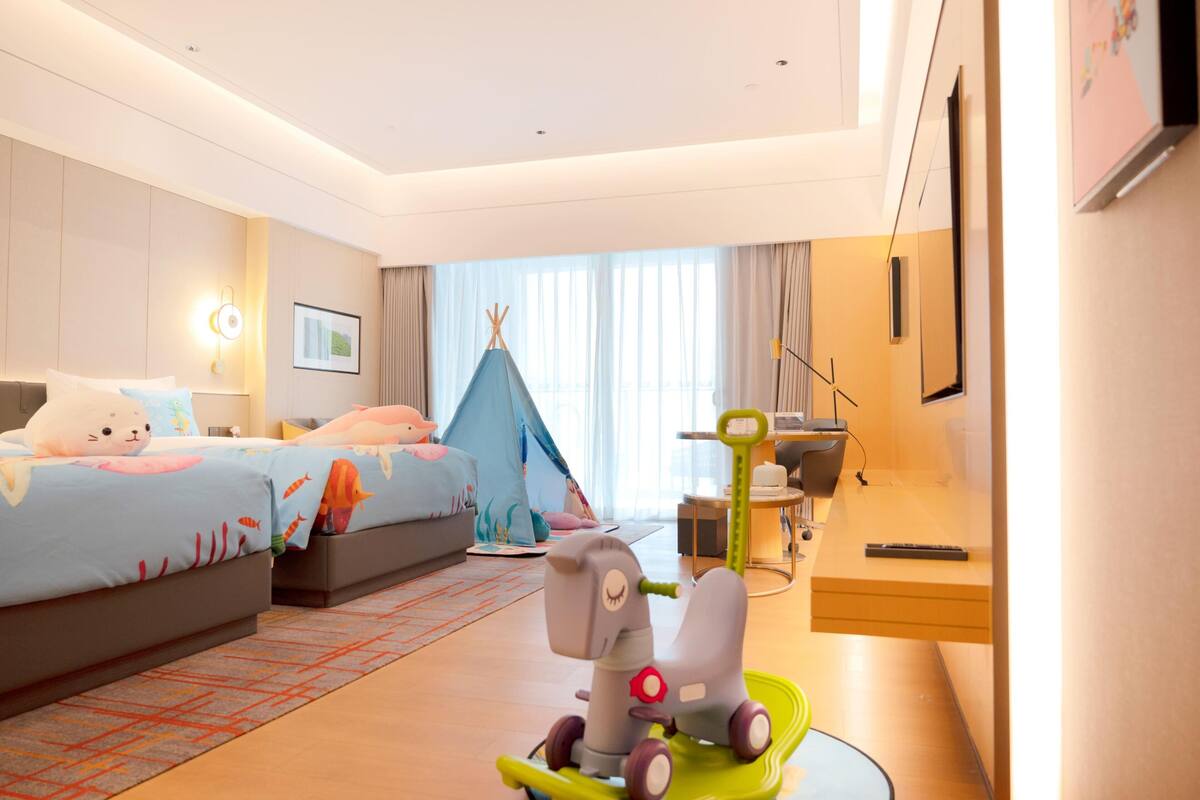 Habitación de hotel con dos camas, una tienda de campaña, un coche de juguete y un escritorio con una silla.