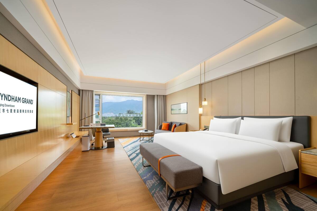 Una habitación de hotel moderna con una cama grande, un escritorio y una pantalla de televisión que muestra el nombre del hotel.