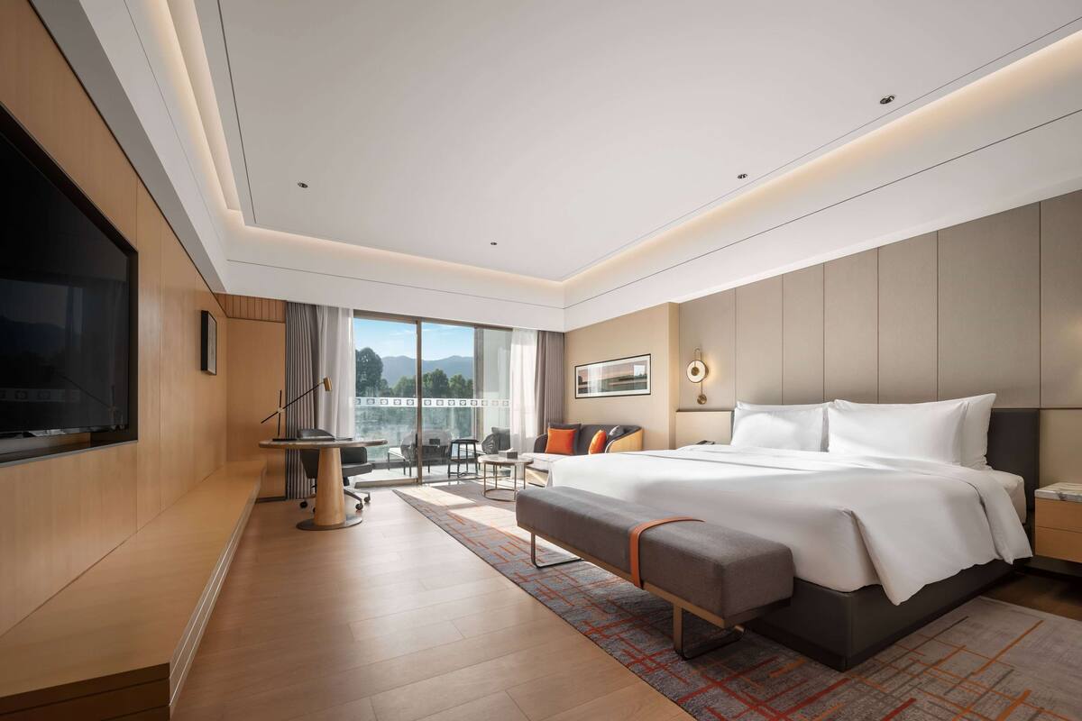 Una habitación de hotel moderna con una cama grande, un televisor, un balcón con vistas y un área de comedor.