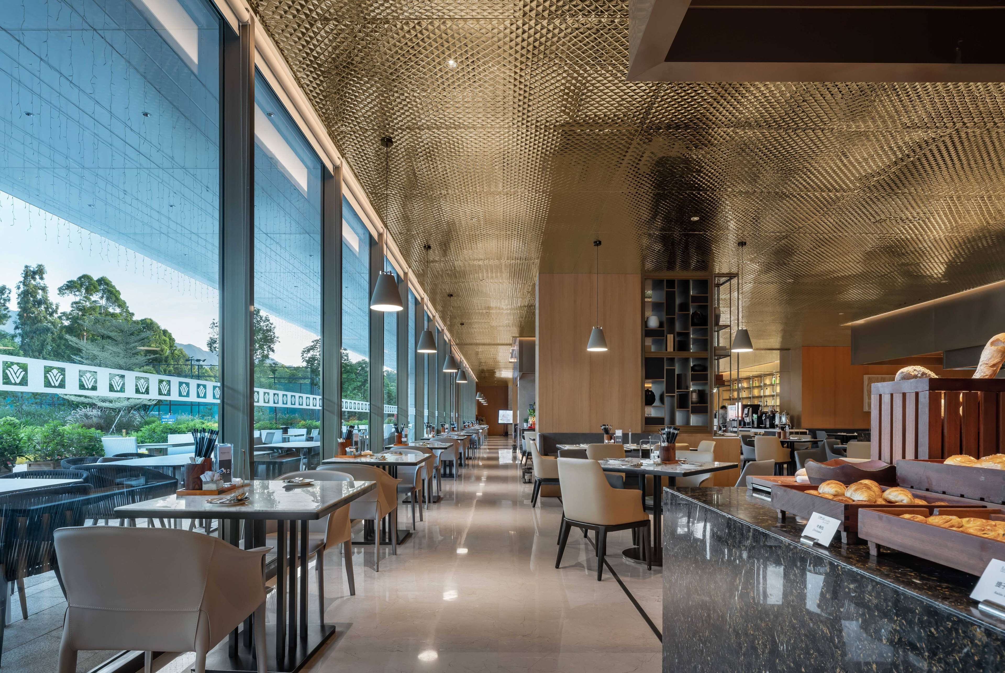 Een modern restaurant met een lange balie, een zithoek en uitzicht op groen buiten.
